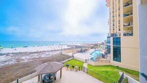 A balcony with a view of a beach, a pool area, and a building with multiple balconies.