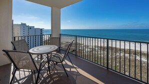 A balcony with a table and chairs, overlooking a beach and ocean.