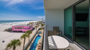 Un balcón con vista a la playa, una piscina y un edificio rosa.