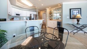 Une cuisine moderne avec des meubles blancs, un îlot central et un coin repas comprenant une table et des chaises en verre.