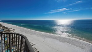 Une vue sur la plage depuis un balcon, avec un ciel dégagé et un soleil éclatant se reflétant sur l’eau.