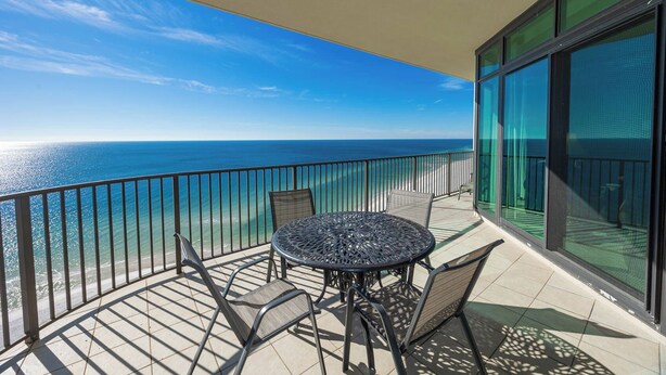 Un balcon avec une table ronde et des chaises, donnant sur une plage et l’océan.