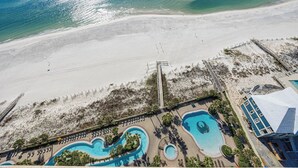 Vue aérienne d’un complexe hôtelier en bord de mer, avec plusieurs piscines, une plage et une jetée.