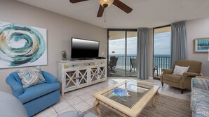 A living room with a TV, sofas, a coffee table, and a balcony with a view of the sea.