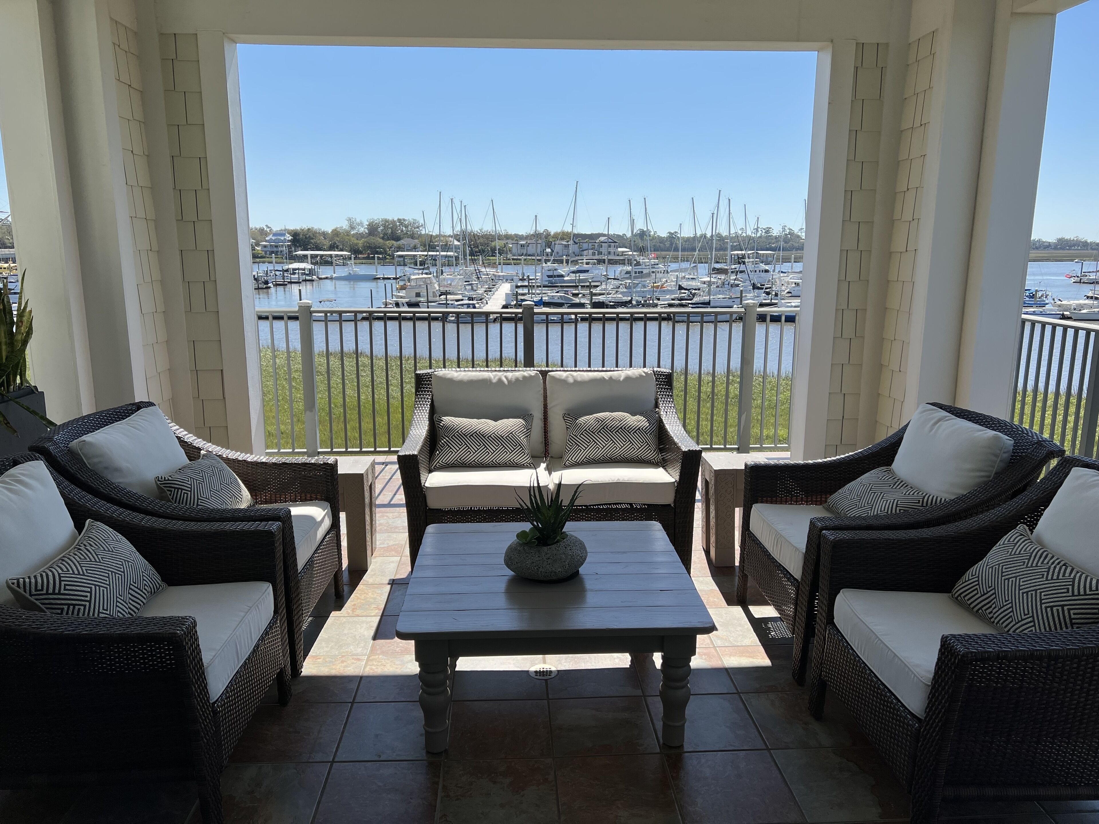 Een overdekt terras met rieten meubilair en uitzicht op een jachthaven.