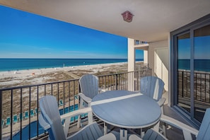 Un balcón con vista a la playa, una piscina y mobiliario exterior.