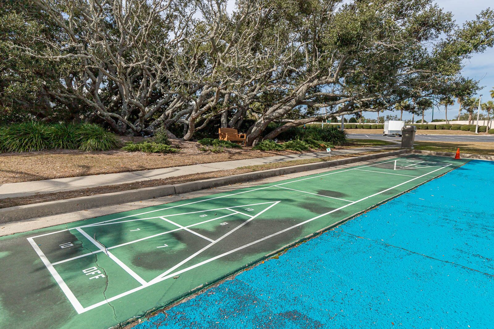 A shuffleboard court adjacent to a pool with a tree-lined background.
