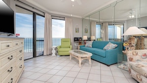 A spacious living room with a large window, a green armchair, a blue sofa, and a glass coffee table. - Cozy 2BR Condo - Phoenix VII 71109 (Orange Beach)