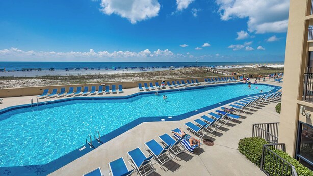 A large pool with blue water, surrounded by lounge chairs and a view of the beach and ocean.