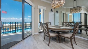 A dining area with a round table and chairs, a view of a pool and beach, and a ceiling light fixture.