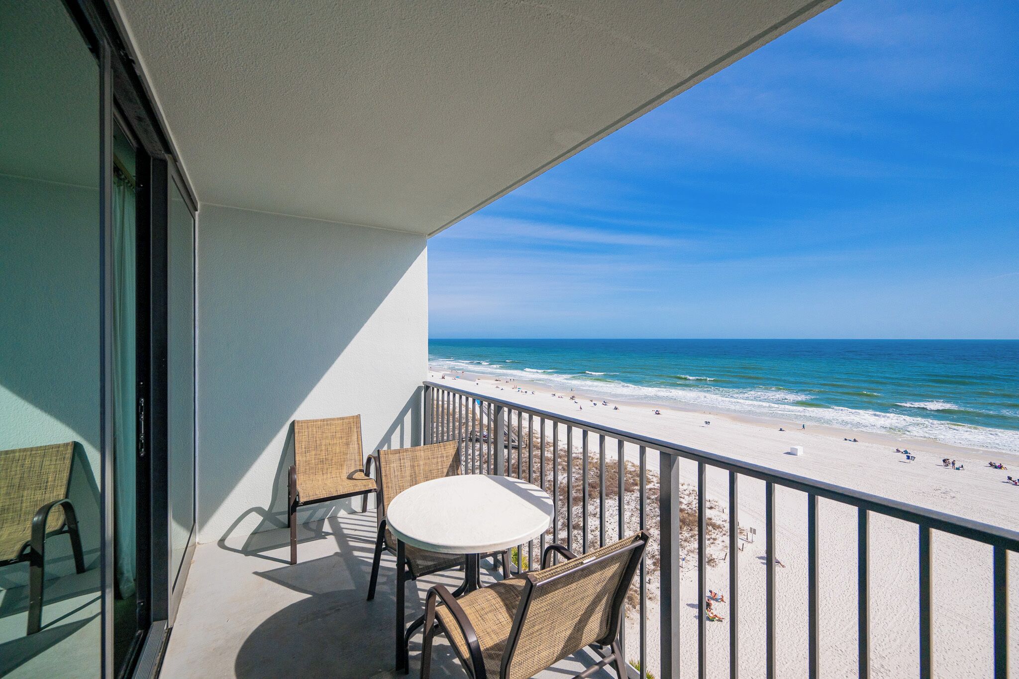 A balcony with a table and chairs, overlooking a beach with people and the ocean.