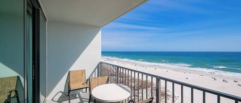 A balcony with a table and chairs, overlooking a beach with people and the ocean.