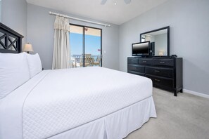 A hotel room with a large bed, a TV, a dresser, and a balcony with a view.