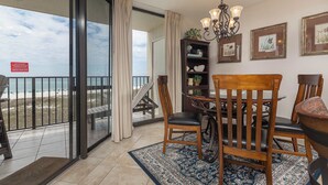 A balcony with a view of the beach, a dining area with wooden chairs and a table, and a chandelier.