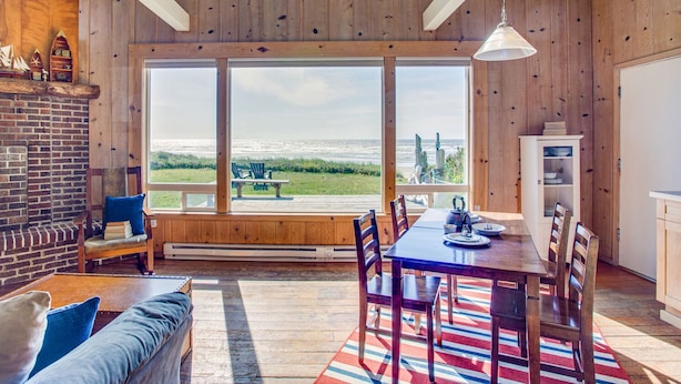 Ein Zimmer mit großem Fenster mit Blick aufs Meer, einem Esstisch mit Stühlen, einem Kamin und einer Holzbalkendecke.