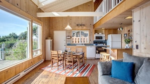 Ein gemütliches Blockhaus mit Essbereich, Küche und einem grauen Sofa mit blauen Kissen.