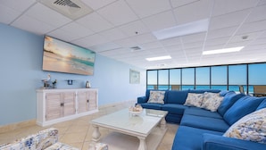 A modern living room with a large window, a blue sofa, a white coffee table, and a cabinet with decorative items.