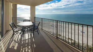 A balcony with a table and chairs, overlooking a beach and the sea.