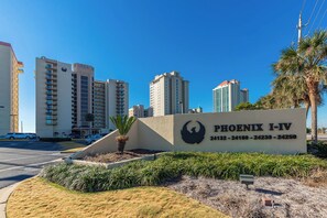 Une enseigne pour Phoenix I-IV, avec un logo représentant un oiseau, entourée d’un espace paysager agrémenté de palmiers et d’un parking.