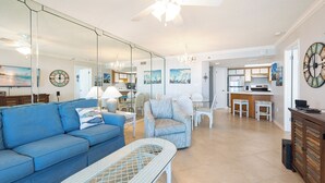Ein Wohnzimmer mit blauem Sofa, einem Korbtisch und einem Essbereich mit weißen Stühlen und einem Tisch.