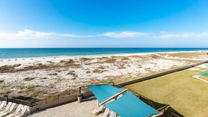 Strandudsigt med klart skyn, sandstrand og græsareal med liggestole og parasoller.