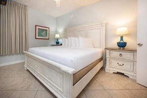 Een slaapkamer met een groot bed, een nachtkastje met een lamp, een dressoir, een inlijstend schilderij aan de muur en een raam met gordijnen.