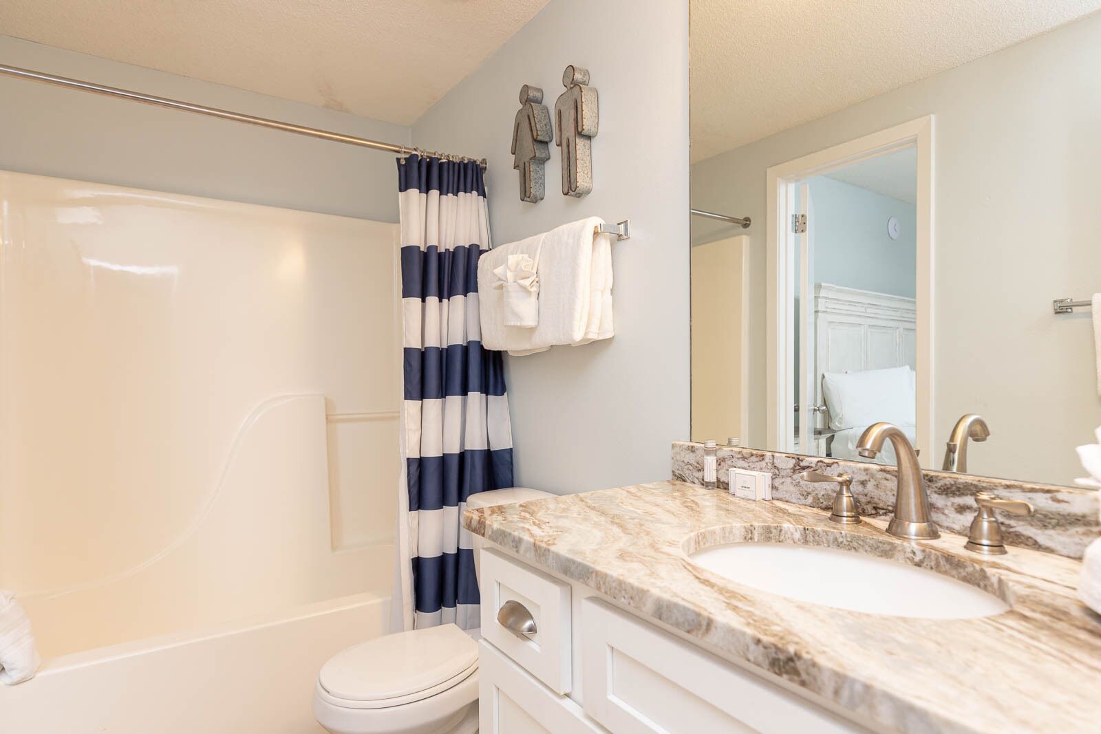 Une salle de bain comprenant une baignoire, un rideau de douche, des toilettes, un lavabo avec un plan de toilette en marbre et un miroir.