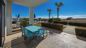 A covered patio area with a turquoise table and chairs, palm trees, and a view of a parking lot.