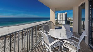 Un balcon avec une table et des chaises donnant sur une plage et l’océan.
