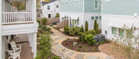 Un barrio residencial con un sendero pavimentado, una terraza de madera y un patio cercado con diversas plantas.