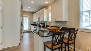 Una cocina moderna con armarios blancos, encimera de granito y una isla central con dos taburetes de bar.
