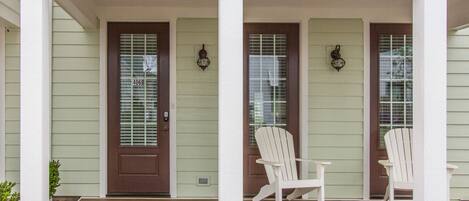A house with a porch, a door marked 406B, and two white Adirondack chairs.