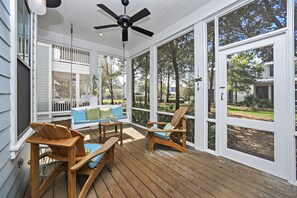 Eine überdachte Veranda mit Holzterrasse, Deckenventilator, einem weißen Sofa mit blauen Kissen und einem Holzstuhl.