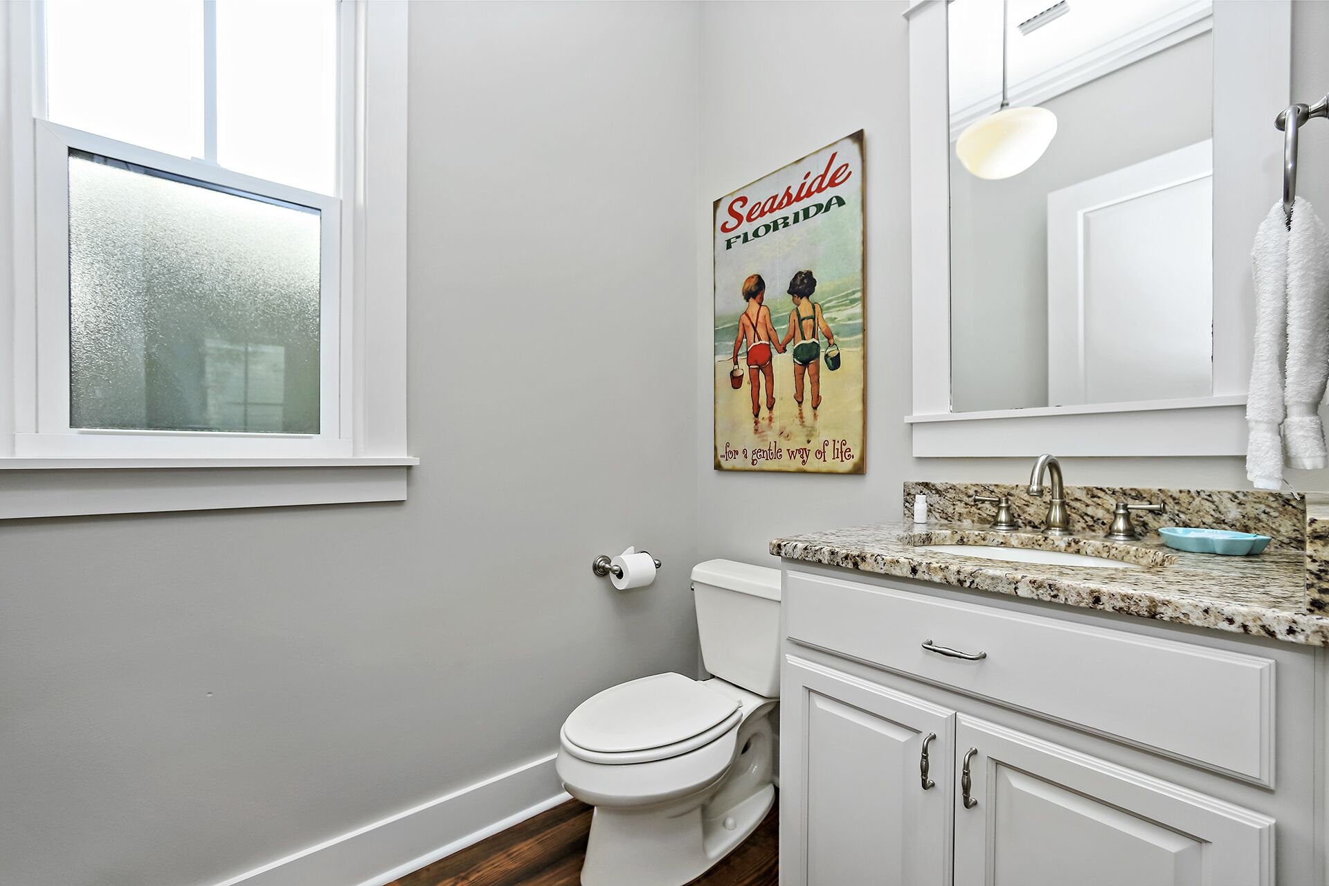 Une salle de bain avec des toilettes, un lavabo et une affiche représentant deux personnes sur une plage.
