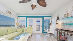 Una sala de estar con vista a la playa, un ventilador de techo y un televisor.