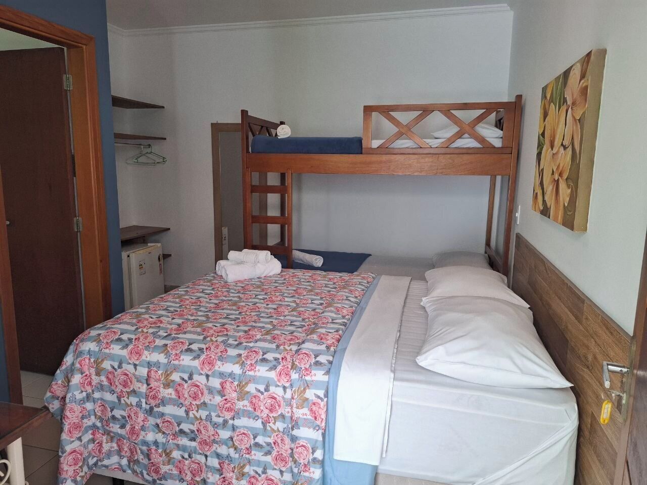 A bunk bed with a floral bedspread, a wooden headboard, and a small shelf with a hanger.