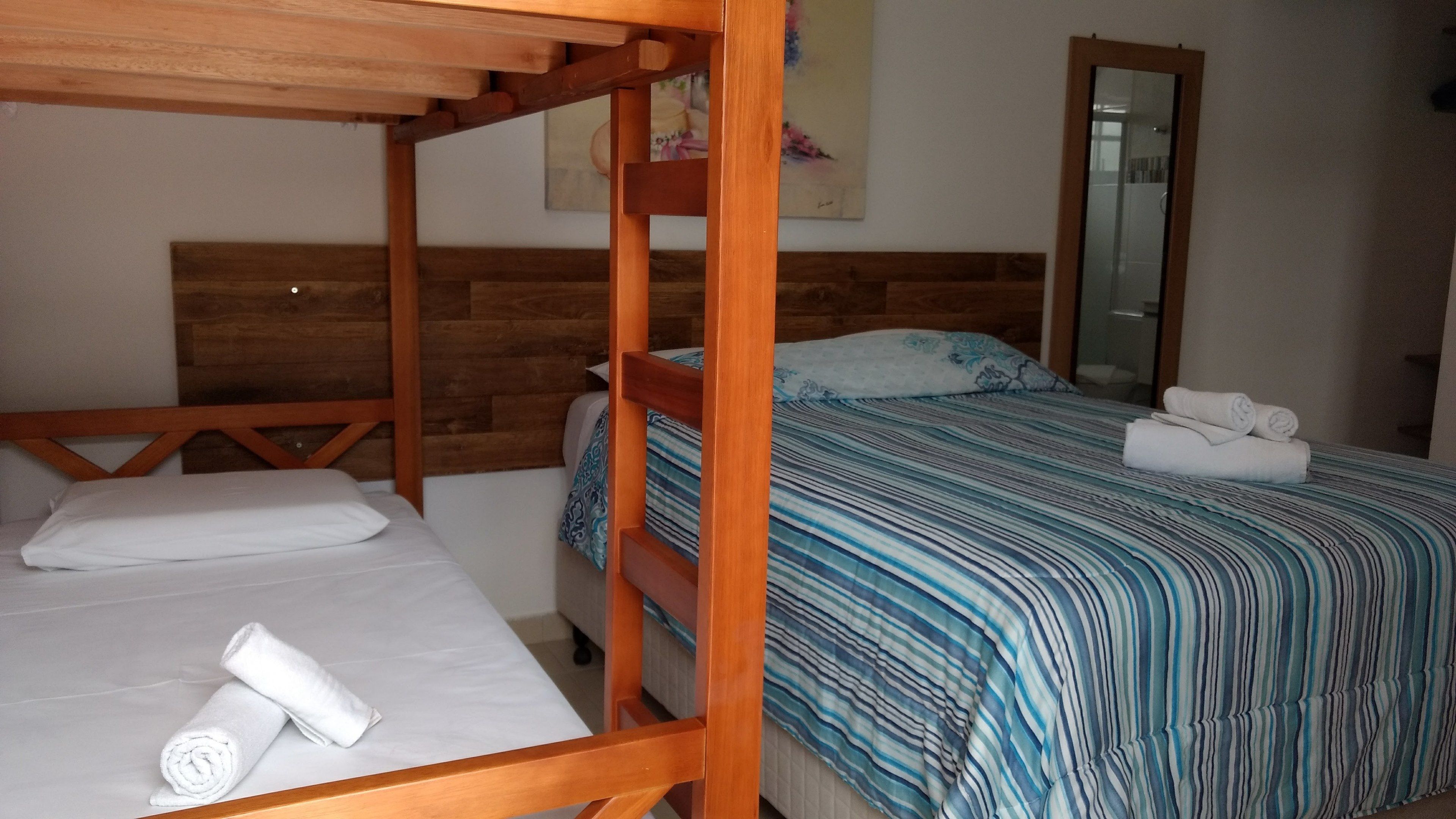 A room with a bunk bed, a single bed, and a large mirror.