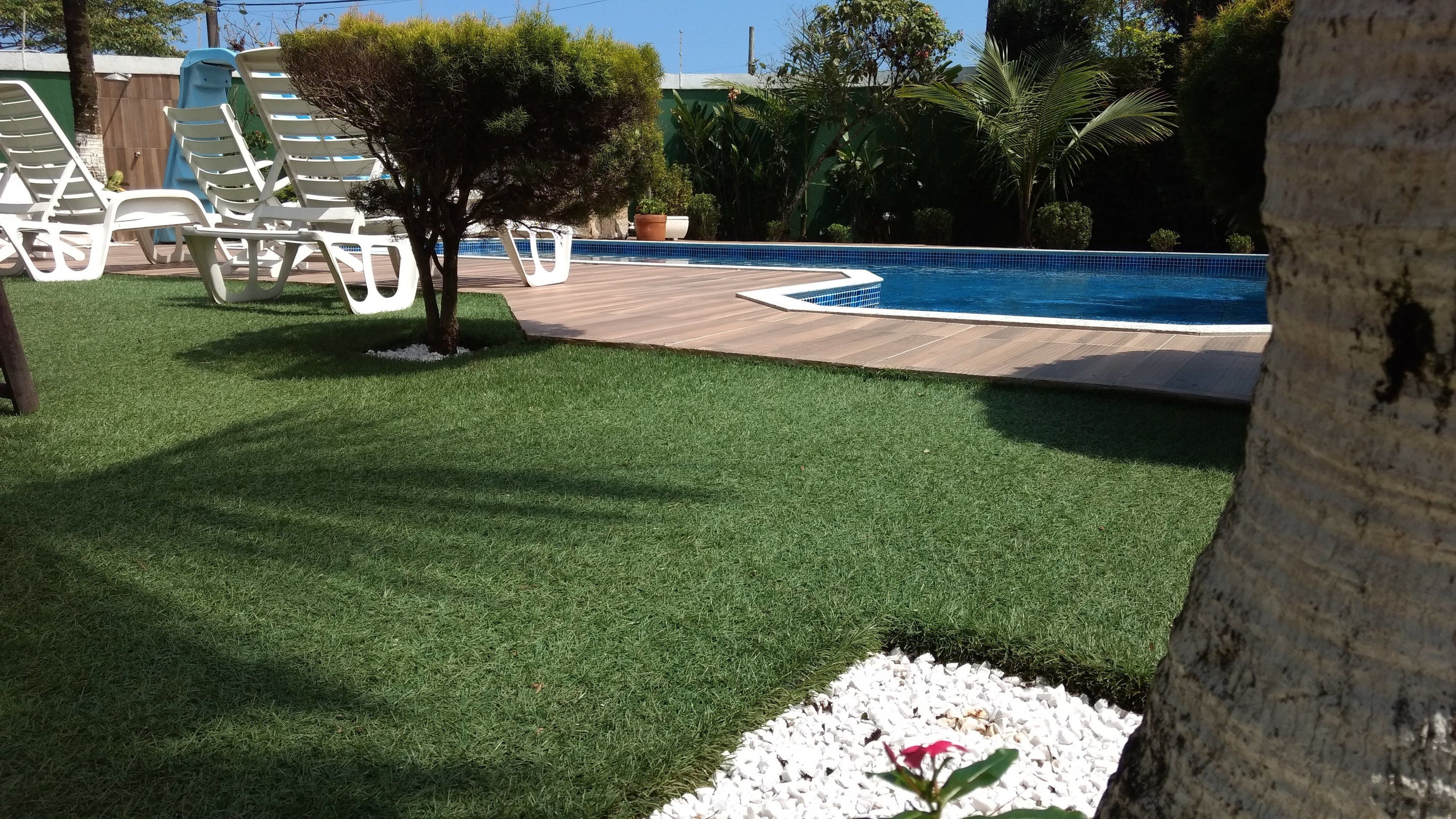 Zona de piscina con césped artificial, sillas de lounge blancas y una terraza de madera.