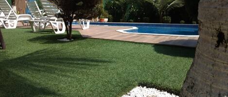 A pool area with artificial grass, white lounge chairs, and a wooden deck.