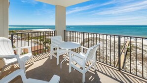 Ein Balkon mit weißen Stühlen und einem Tisch, der einen Blick auf einen Strand und das klare Meer bietet.