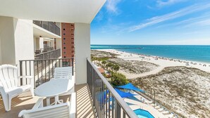 Ein Balkon mit Blick auf einen Strand, Sitzgelegenheiten im Freien und einem Poolbereich.