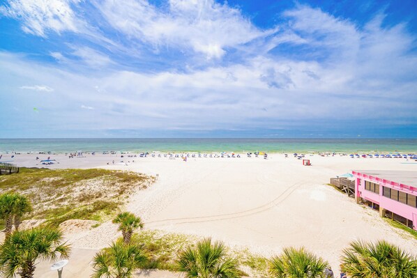 Ein Strand mit einem rosafarbenen Gebäude, Palmen und blauem Himmel.