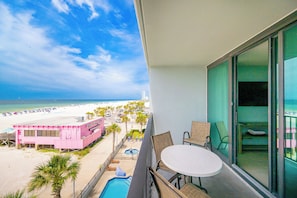 Ein Balkon mit Blick auf einen Strand, ein Schwimmbad und ein pinkfarbenes Gebäude.
