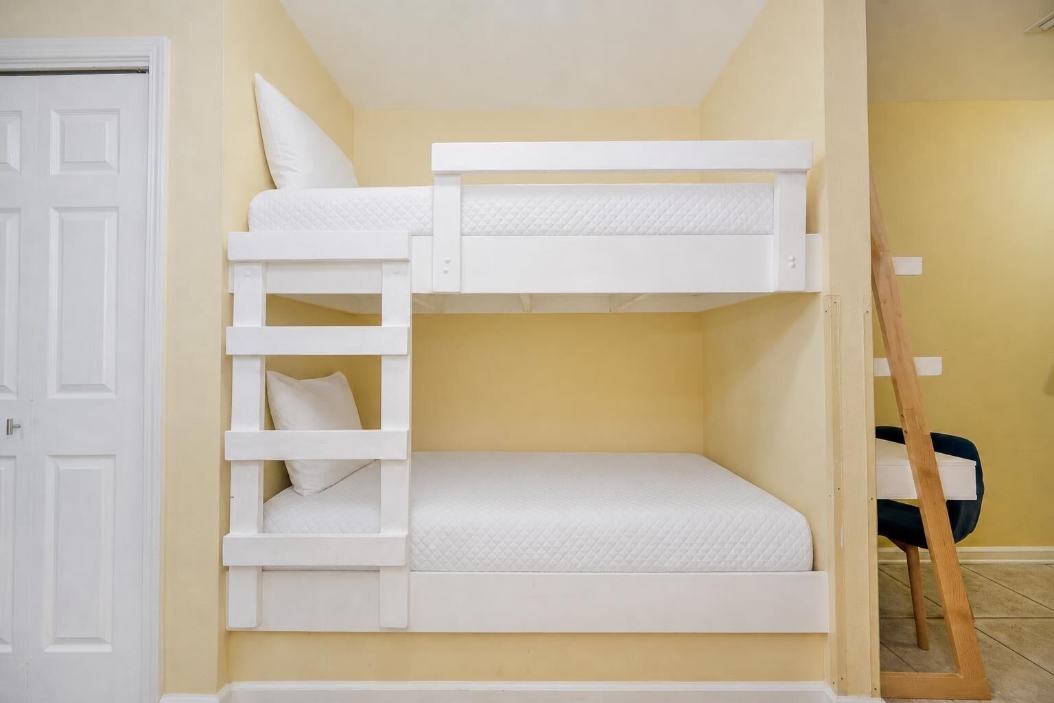 A bunk bed with a ladder, a white door, and a wooden ladder leaning against the wall.