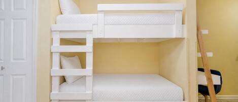 A bunk bed with a ladder, a white door, and a wooden ladder leaning against the wall.
