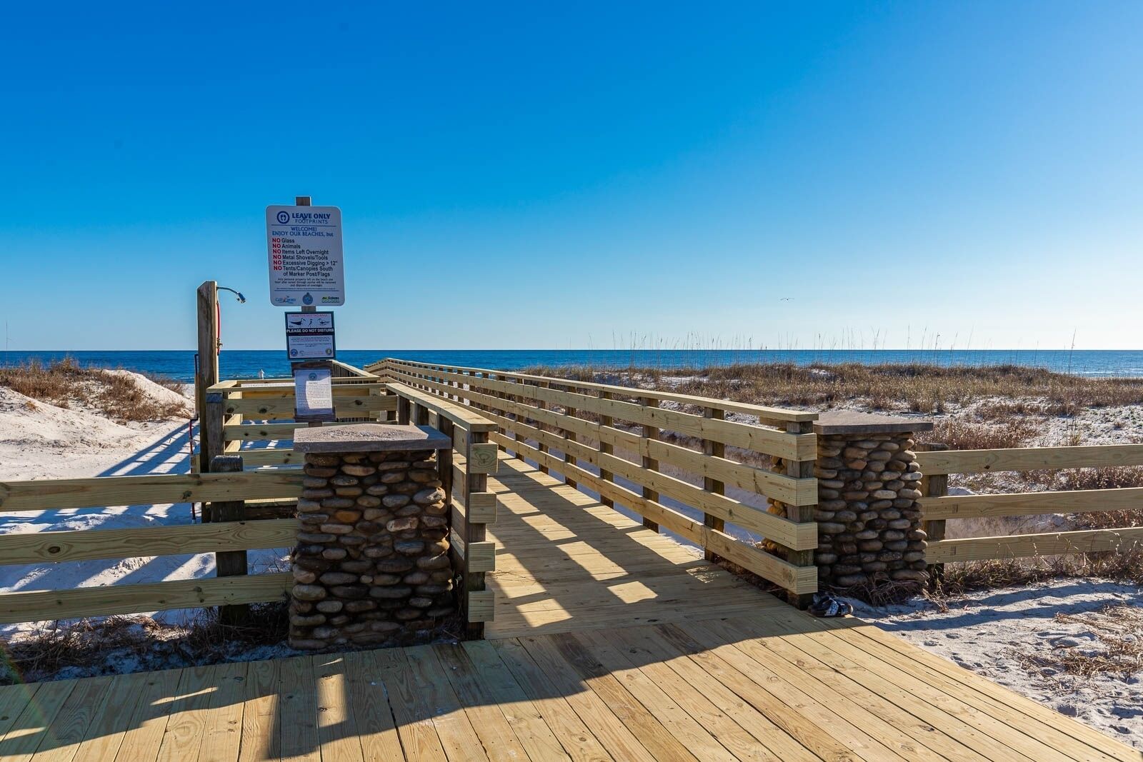 A wooden boardwalk leading to a beach with a 'Leave Only Trash' sign.