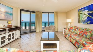 A living room with a view of the beach, a ceiling fan, a sofa, a coffee table, and a TV.