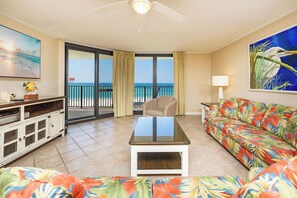 A living room with a view of the beach, a ceiling fan, a sofa, a coffee table, and a TV.