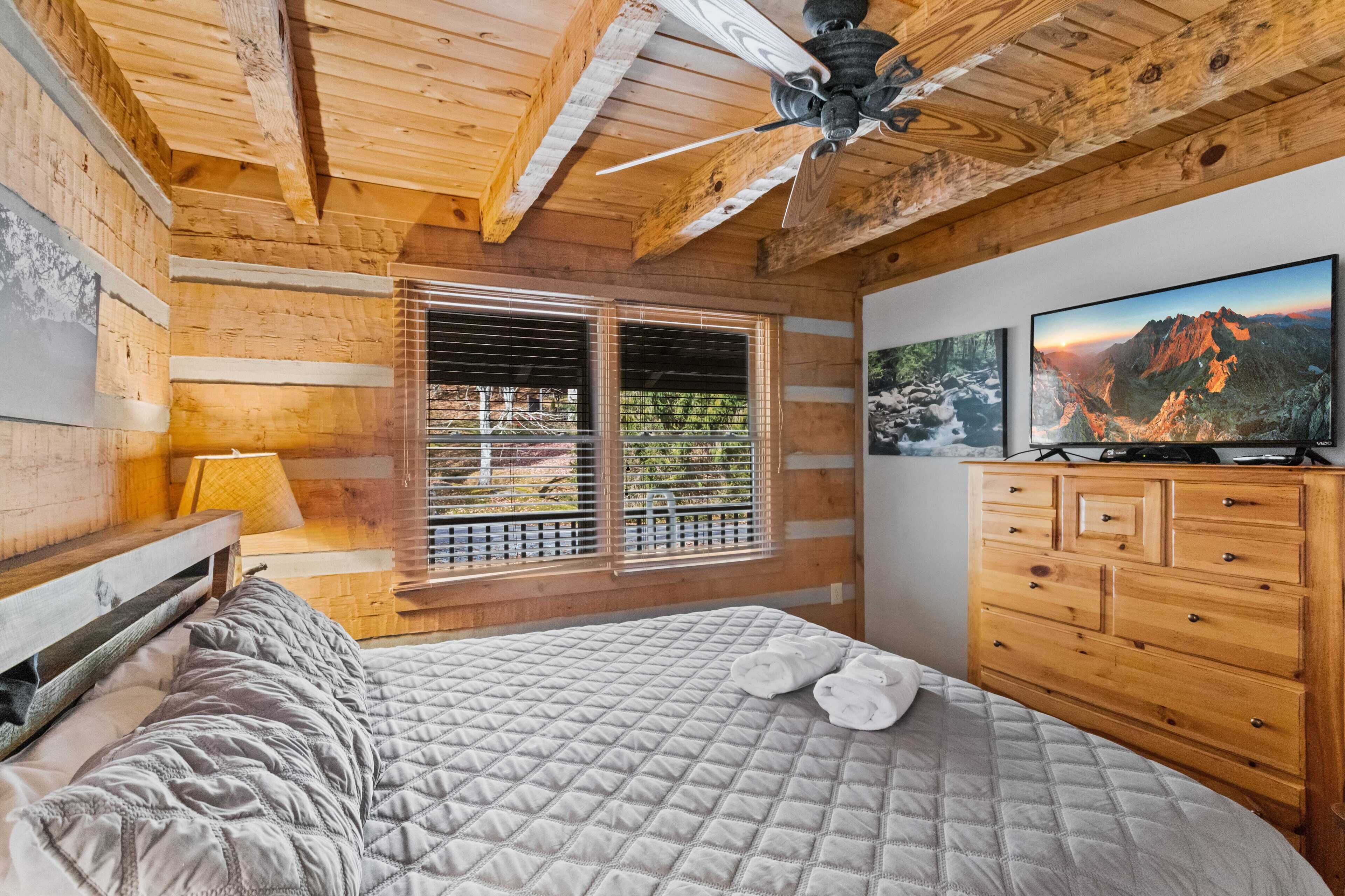 A wooden cabin bedroom with a bed, a dresser, and a television.