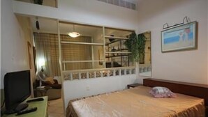 Une chambre à coucher avec un lit, un bureau avec un ordinateur, une fenêtre et un tableau accroché au mur.
